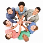 Group of young adults smile up at the camera while standing with their hands together in a circle. Horizontal shot. Isolated on white.